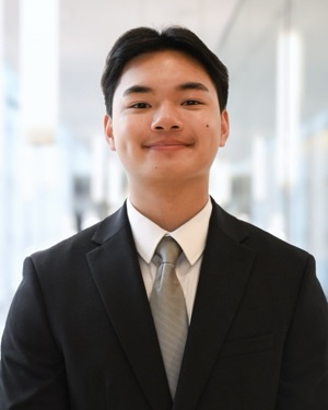 Jonathan Chau in a dark suit and grey tie, photographed in a glass-walled campus building