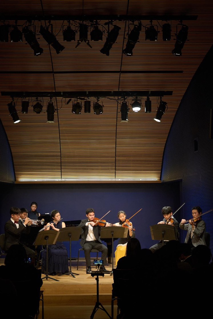 Think Symphony performing on a lit stage: trumpet, flute, violins, viola and piano
